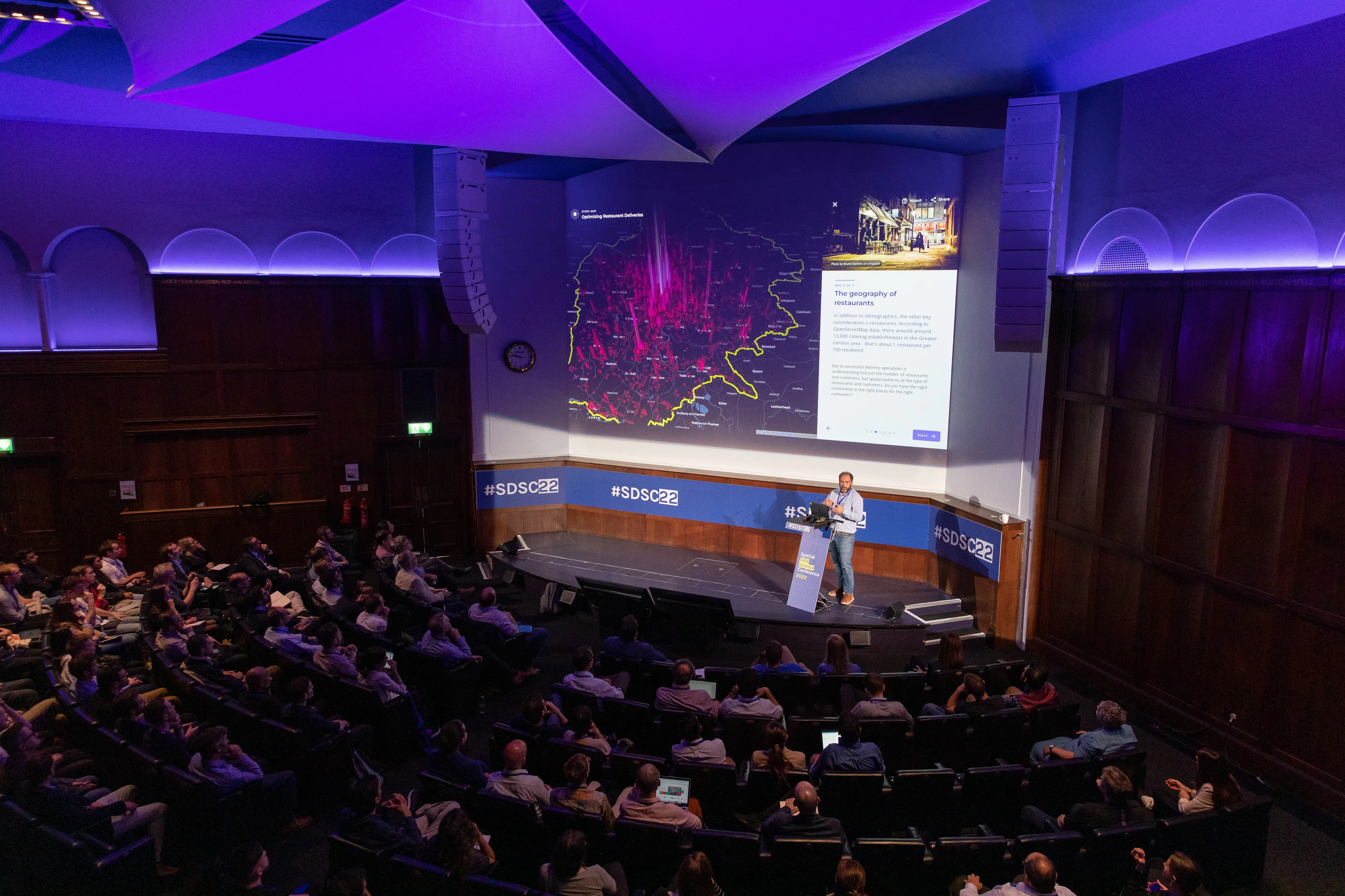A photograph of the keynote presentation from a previous SDSC event, showing the audience, speaker and a map on the screen.